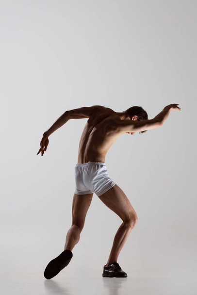 Contemp dance, performance. Young flexible shirtless man in underwear dancing isolated on gray background. Art, music, beauty. Healthy lifestyle concept - Photo, Image