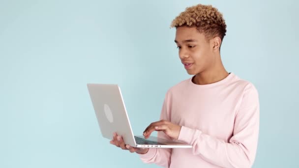 Emocionado adolescente celebrando buenas noticias en el ordenador portátil contra el fondo azul - Imágenes, Vídeo