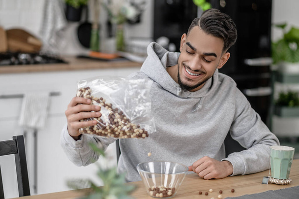 A smiling man in a grey hoodie making breakfast - Fotoğraf, Görsel