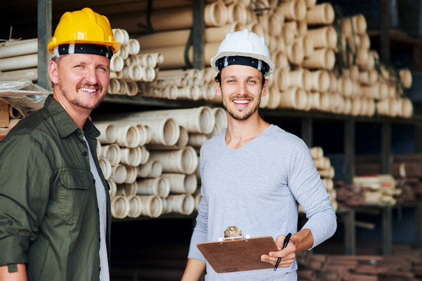 Sou o homem com o plano. Retrato recortado de dois trabalhadores da construção do sexo masculino olhando sobre alguma papelada enquanto em pé em um armazém industrial. - Foto, Imagem