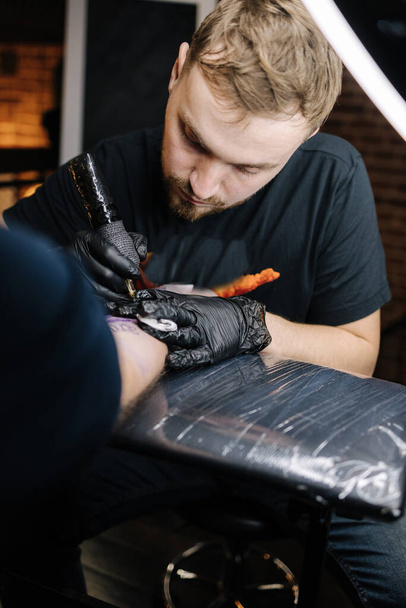Il maestro del tatuaggio sta tatuando una mano di un uomo. Macchina senza fili del tatuaggio, sicurezza e igiene sul lavoro. Primo piano del lavoro del tatuatore. Salone del tatuaggio - Foto, immagini