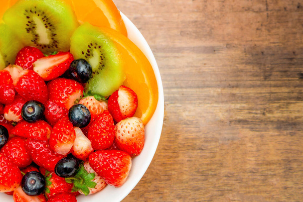 concepto de frutas frescas, ensalada de frutas consisten en kiwi y bayas surtidos en un tazón sobre fondo de madera. - Foto, Imagen