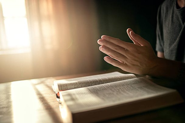 Zaczyna dzień we właściwy sposób. Przycięte ujęcie niezidentyfikowanego mężczyzny ściskającego dłonie w modlitwie o otwartą Biblię. - Zdjęcie, obraz