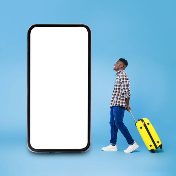 青い背景の上に大きな電話の近くに立つアフリカ人旅行者の男 - 写真・画像