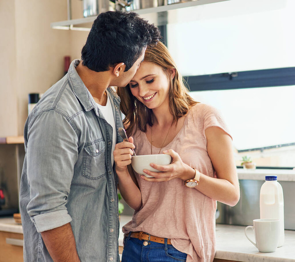 Enjoying the food...and the kisses. Shot of an affectionate young couple standing in their kitchen. - 写真・画像
