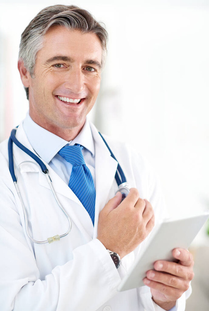 De resultaten zijn binnen. Portret van een arts die een digitale tablet vasthoudt terwijl hij in een ziekenhuisgang staat. - Foto, afbeelding