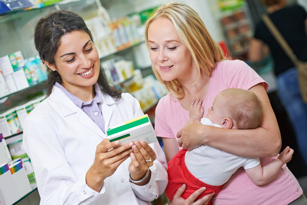 Iloinen apteekkarin työntekijä antaa vitamiineja äidille, jolla on lapsi apteekissa apteekissa - Valokuva, kuva