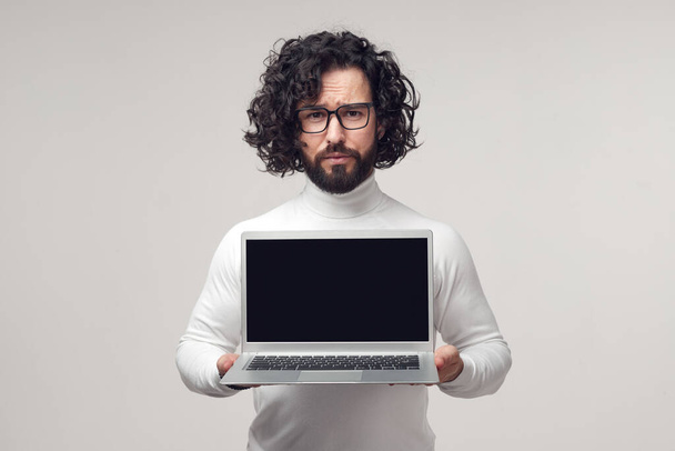Unsure bearded man showing laptop with empty black screen - Foto, Imagem