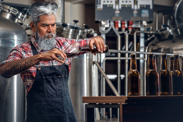 Alter Mann gießt in moderner Brauerei Bier ins Glas - Foto, Bild