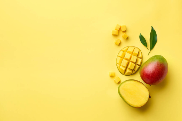 Verse hele helft en gesneden mango fruit op gele achtergrond, bovenaanzicht, platte lay, kopieer ruimte voor tekst - Foto, afbeelding