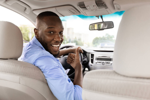 Feliz hombre negro sentado en el coche mostrando los pulgares hacia arriba gesto - Foto, Imagen