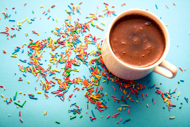 Una taza de café negro caliente sobre fondo azul con coloridas salpicaduras de azúcar. - Foto, imagen