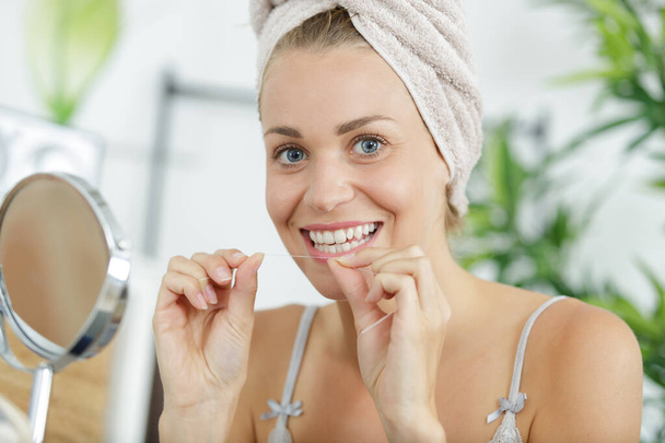 smiling beautiful woman in bath towel using a dental floss - Fotografie, Obrázek