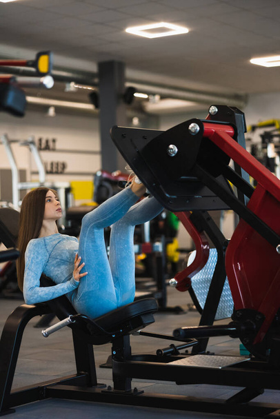 Jonge vrouw doet fitnesstraining op een beenverlenger push machine met gewichten in een fitnessruimte. Meisje schudt beenspieren - Foto, afbeelding