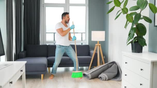 Muž uklízí dům a baví se tancováním s koštětem - Záběry, video