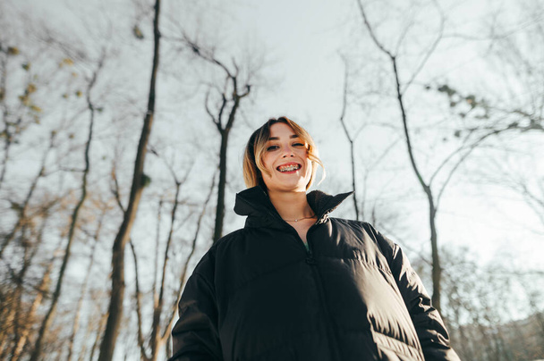 Portré gyönyörű elegáns nő fogszabályzóval a téli parkban, nézi a kamera és a mosolygós. - Fotó, kép