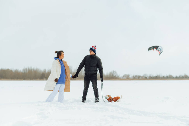 Family with a dog on a leash standing holding hands during a winter walk and with a smile on their faces looking at each other and smiling - Foto, imagen