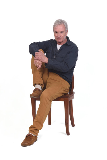Mann sitzt auf Stuhl mit Fuß auf Stuhl auf weißem Hintergrund - Foto, Bild