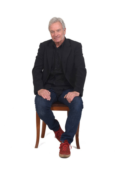 front view of a man sitting  on chair with sneakers jeans and blazer on white background - Photo, image