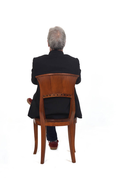 vue arrière d'un homme assis sur une chaise avec des baskets jeans et blazer, bras et jambes croisés sur fond blanc - Photo, image