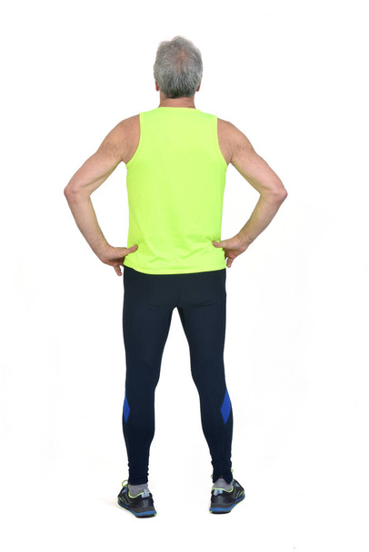 vista posterior de un hombre en medias de ropa deportiva y amarillo fluorescente, manos en la cadera sobre fondo blanco  - Foto, imagen