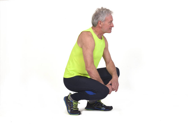 side view of a senior man with sportswear squatting on white background - Foto, immagini