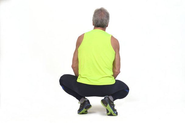 back view of a senior man with sportswear squatting on white background - Фото, изображение