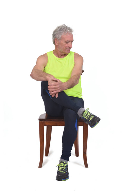 vista frontal de un hombre en medias de ropa deportiva y fluorescente amarillo sin mangas sentado en la silla mirar hacia abajo sobre fondo blanco  - Foto, imagen
