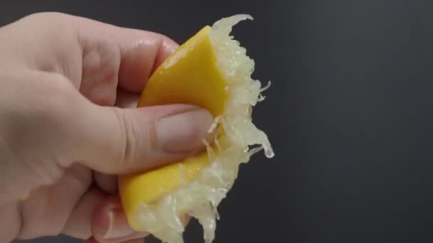 黒の背景にレモンの半分を絞る手。ライムドロップでライムを手絞る。スタジオ4Kビデオ映像で手にレモン汁を押してスクワット。酸っぱくて爽やかなドリンクメニューを代表する. - 映像、動画