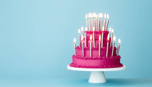 Bolo de aniversário em camadas rosa extravagante com muitas velas de aniversário de ouro contra um fundo azul - Foto, Imagem