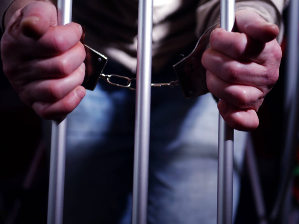 Заключенный в наручниках через тюремные решетки крупным планом  - Фото, изображение