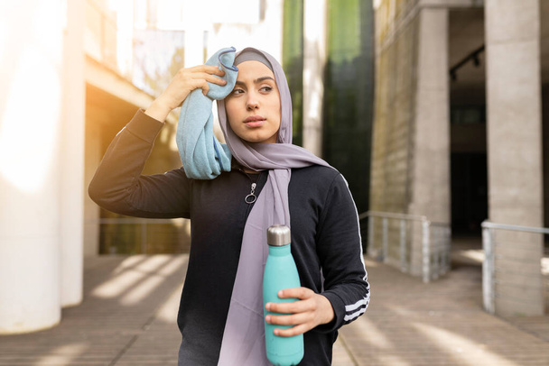Muslimská sportovkyně nosí hidžáb odpočinku po tréninku a utírá pot v parku - Fotografie, Obrázek