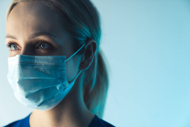 retrato de una hermosa rubia joven enfermera caucásica con una máscara quirúrgica primer plano fondo azul estudio tiro concepto médico - Foto, imagen