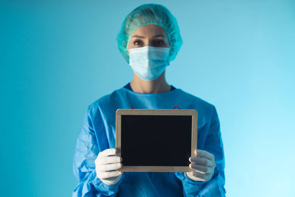 female doctor holding a blank blackboard medium closeup blue background indoor medical concept - 写真・画像