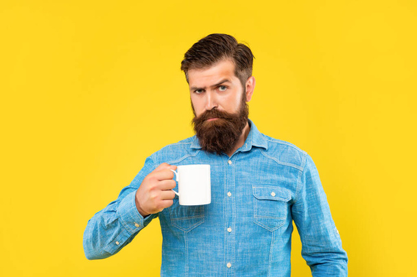 Serious caucasian guy holding tea mug yellow background - Фото, зображення