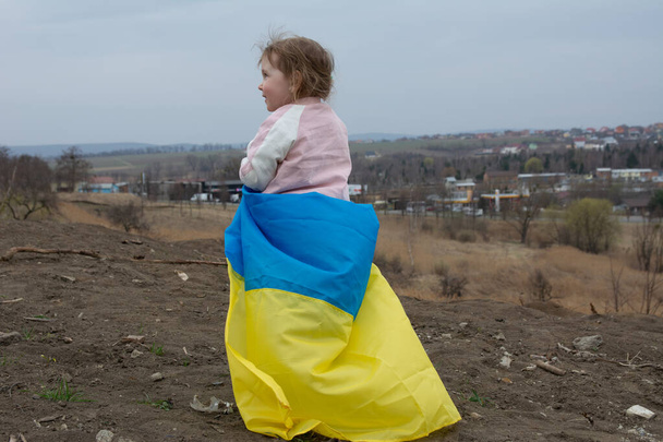 Krásná holčička s vlajkou Ukrajiny na pozadí města a jezera v ukrajinském městě. Portrét vlastenecké holčičky s vlajkou Ukrajiny. - Fotografie, Obrázek