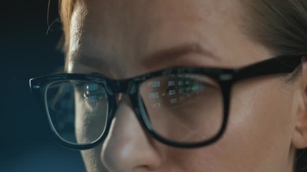 Mujer con gafas mirando el monitor y trabajando con datos y análisis. La pantalla del monitor se refleja en las gafas. Trabaja de noche. Primer plano extremo - Imágenes, Vídeo