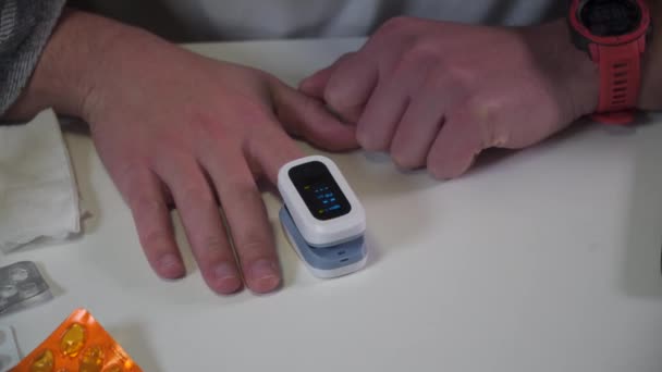 Молодой кавказский мужчина использует монитор насыщения крови кислородом для определения уровня SpO2 в крови во время коронавирусной эпидемии дома, получив плохой результат, стресс и вызывает врача 911. Ковид 19 - Кадры, видео