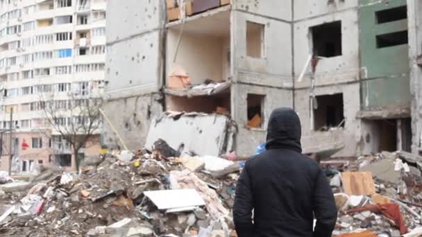 Rückansicht eines Mannes, der nach einem Luftangriff der russischen Armee auf die Ukraine vor einem zerstörten Gebäude steht. Ein zerstörtes Gebäude nach einem Raketenangriff in der ukrainischen Stadt Tschernihiw. - Filmmaterial, Video
