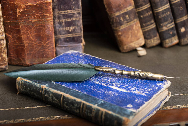 Eski tüy kalem, kitap ve vintage InkWell ahşap masa arka plan kitaplık ve ışık ışınları karşı eski ofiste. Kavramsal arka plan üzerinde tarih, eğitim, edebiyat konuları. - Fotoğraf, Görsel
