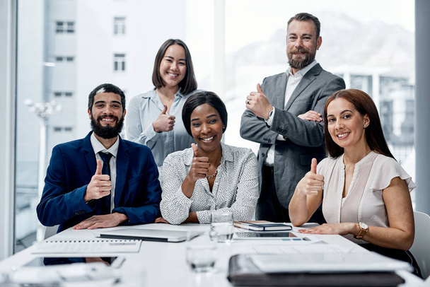A csapatszellem elősegíti a nagyobb teljesítményt. Egy üzletemberekből álló csoport arcképe, akik ujjakat mutogatnak egy irodában.. - Fotó, kép
