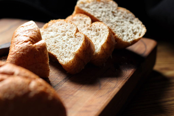 Taze pişmiş ekmek tahta bir kesme tahtasıyla dilimleniyor.. - Fotoğraf, Görsel