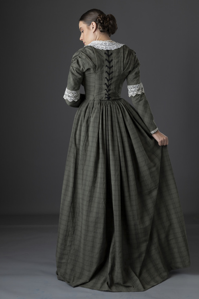 A working class Victorian woman wearing a dark green checked bodice and skirt with a lace collar and standing against a grey studio backdrop - Fotoğraf, Görsel