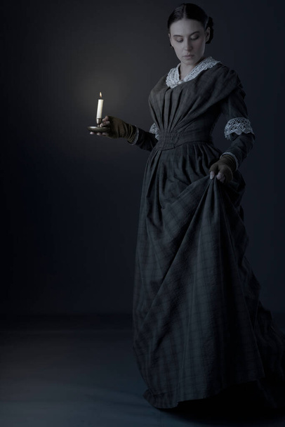Υπηρέτρια ή βικτοριανή εργάτρια φορώντας σκούρο πράσινο καρό μπούστο και φούστα και κρατώντας ένα κερί - Φωτογραφία, εικόνα