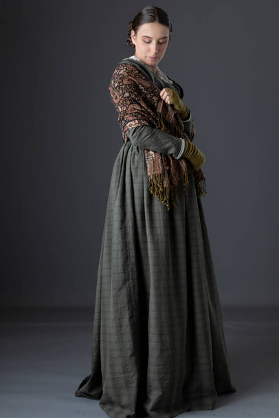 A Victorian working class woman wearing a dark green bodice and skirt with a paisley shawl - Photo, Image
