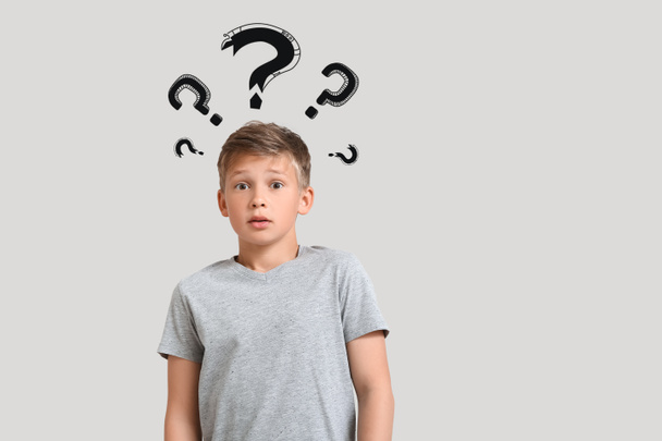 Portrait of shocked little boy and question marks on light background - Foto, Imagen