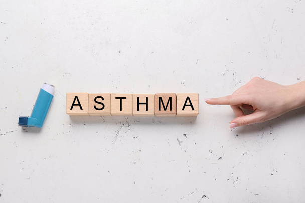 Mano della donna che punta alla parola ASTHMA fatta di cubi di legno su sfondo chiaro  - Foto, immagini