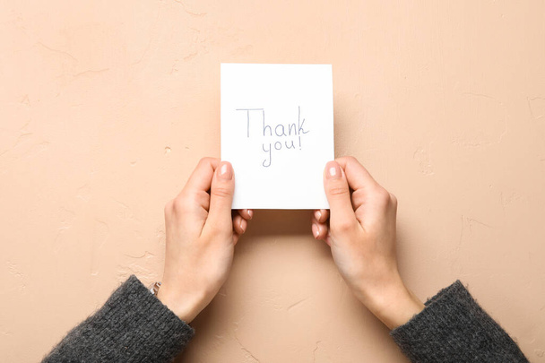 Жінка тримає паперовий аркуш з текстом THANK You на бежевому фоні
 - Фото, зображення