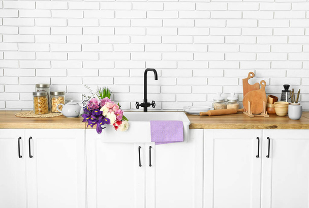 Seramik lavabo, güzel çiçekler ve mutfak gereçleri beyaz tuğla duvarın yanında. - Fotoğraf, Görsel