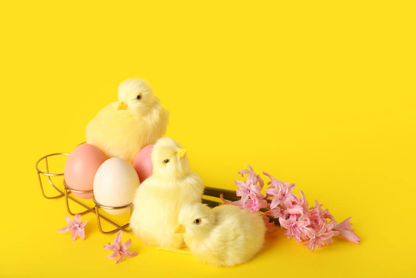Leuke kippen, lentebloemen en paaseieren op gele achtergrond - Foto, afbeelding